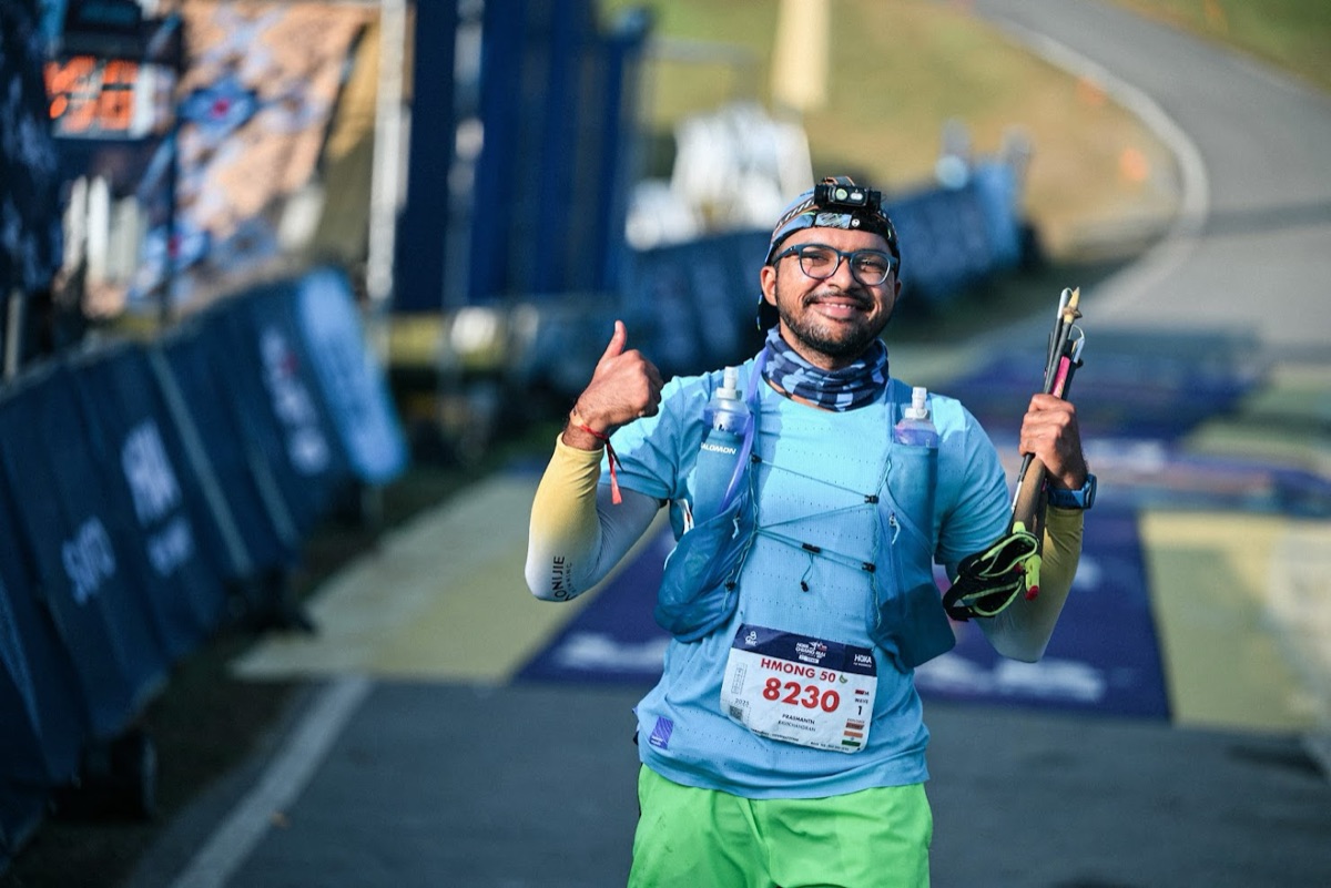 Prashanth Vaidya at the UTMB Chiangmai finish line, smiling with a thumbs up, trekking poles and a hydration vest